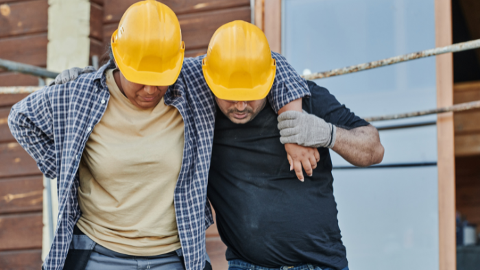 Injured workers Worker with personal injury is helped by another worker wearing a hard hat