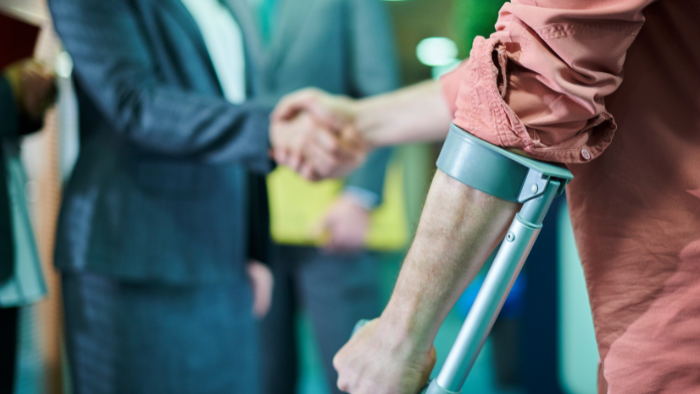 a-person-with-an-arm-crutch-shakes-hands-with-a-person-in-a-suit A person with an arm crutch shakes hands with a person in a suit